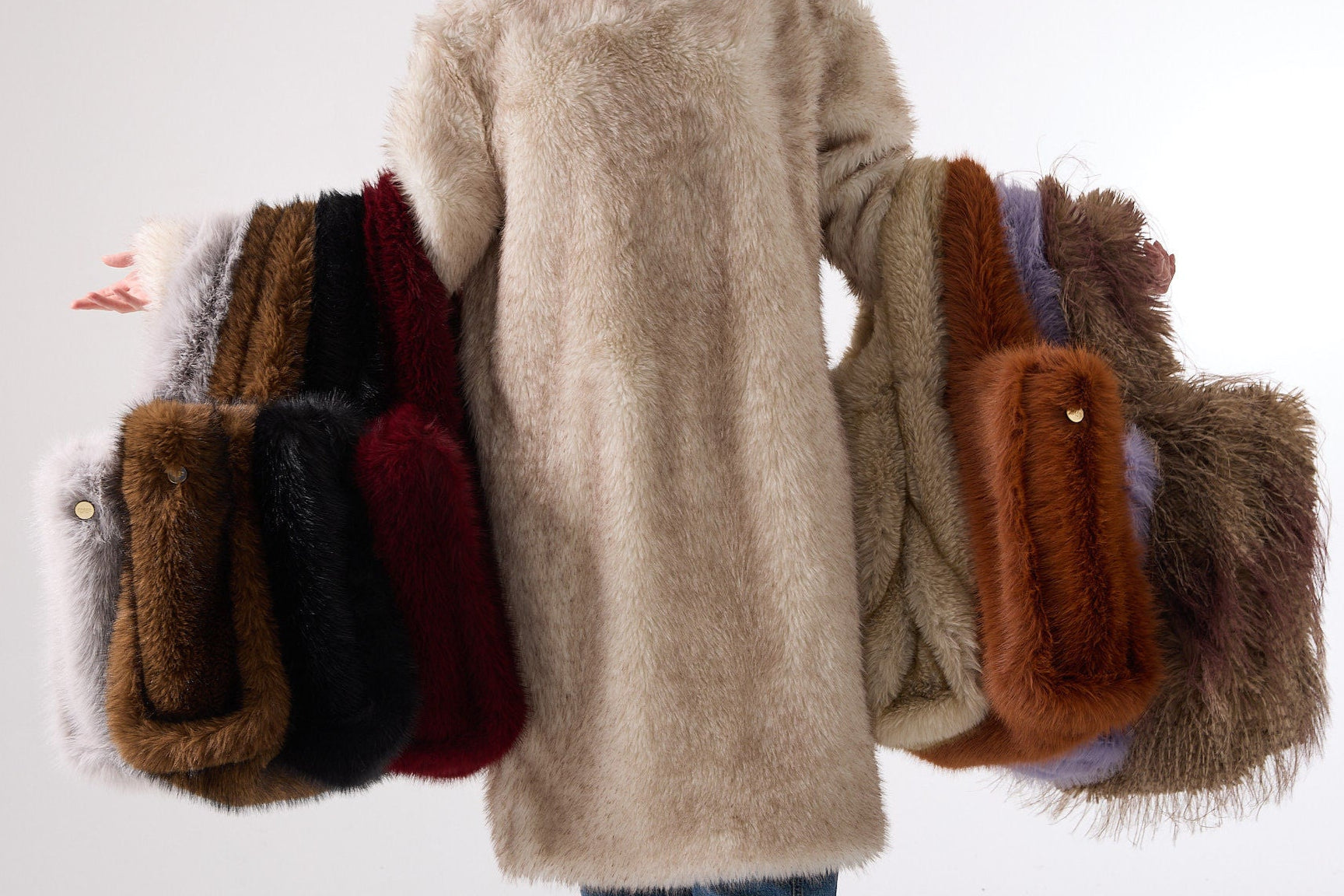 A model in a faux fur coat with both arms full of faux fur tote bags.